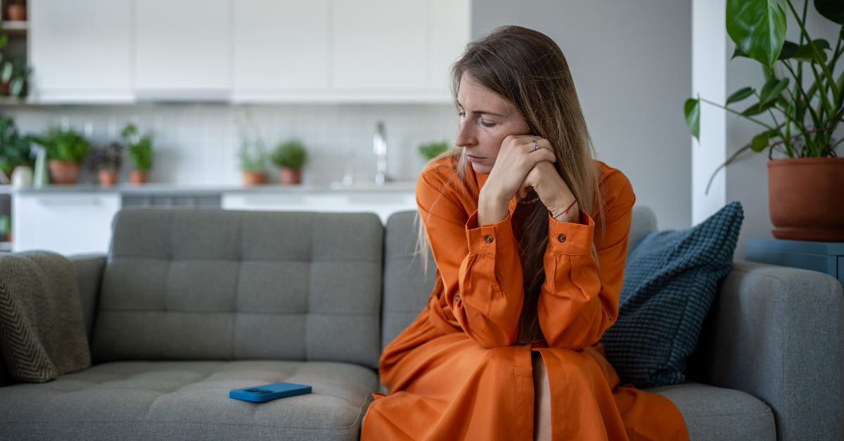 Smutná žena sedí na gauči a pozerá na mobil, ktorý jej pripomína niekoho, kto zmizol bez slova.
